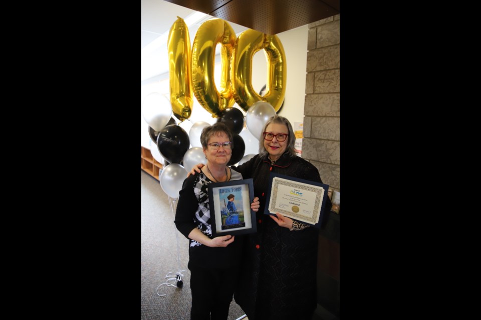 Author Linda Ford, left poses with a book cover and Mayor Judy Dahl displays the certificate from the Town she gave Ford for having published 100 books.