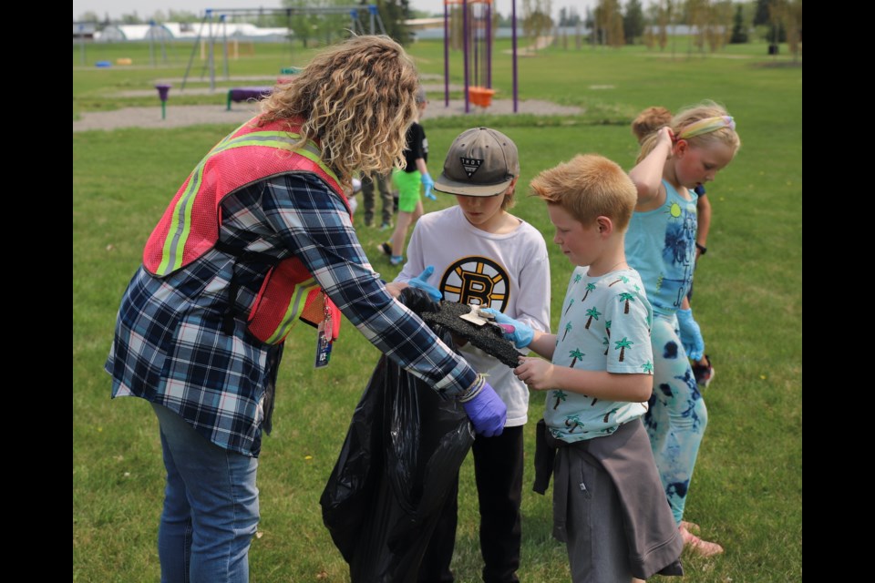 During PUG Day, Olds Elementary School student Rhett Wickwire dumps some of the trash he found in a bag held open by Grade 2 teacher Amanda Koch and Byron French (in hat) while Clara Smith looks for more trash.


