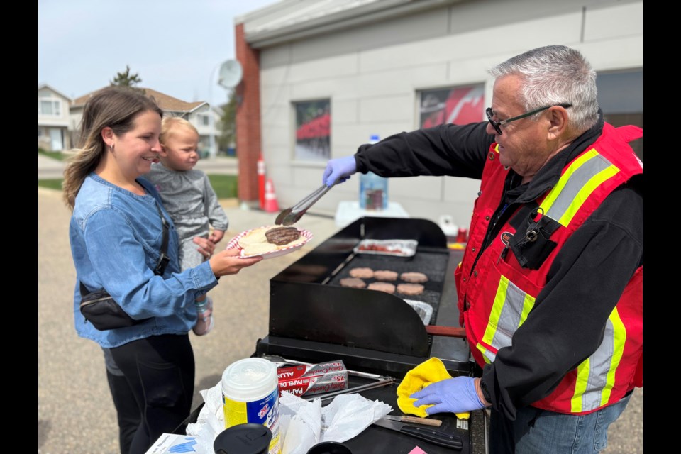A Citizens On Patrol volunteer serves a smiling local mother a hamburger during the Innisfail and Penhold Citizens On Patrol BBQ held on May 9 in the parking lot of the Innisfail RCMP detachment from 11 a.m. to 3 p.m. Johnnie Bachusky/MVP Staff