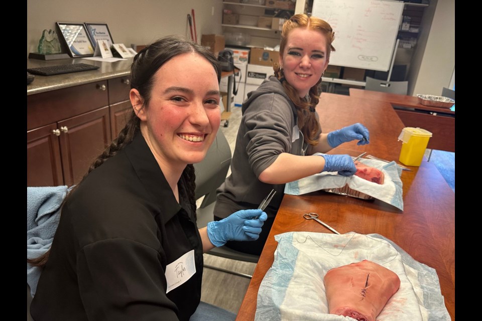 Sundre High School Grade 12 classmates Taylor Hollar, left, and Raelyn Davidson were among a contingent of roughly 40 students, including some from Cremona and Caroline, who on March 13 participated in the annual health-care skills day, which features several stations including one that introduces students to suturing. 
Photo courtesy of Chinook’s Edge School Division