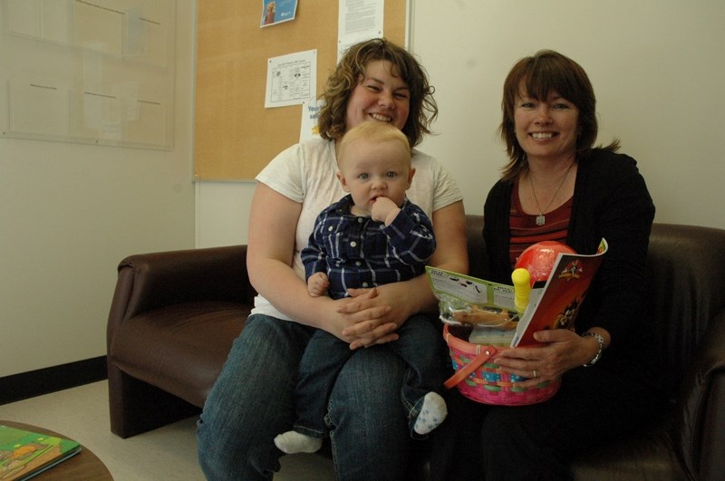 Seven-month-old Corbin and his mom Holly accept a toy gift basket won in a draw at the Sundre Health Clinic. Heather McEwan, speech-language pathologist, right, presents the