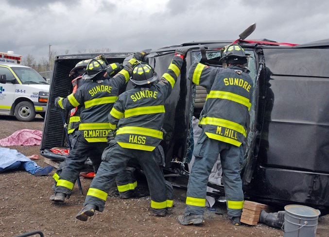  Members of the Sundre Fire Department combine their strength to pull off the truck's roof after using the Jaws of Life to cut it loose.