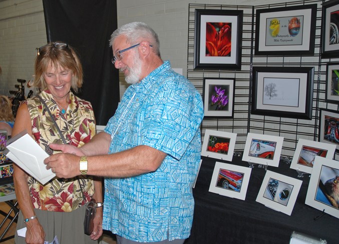  Pat Dahlman, from the James River Bridge area, shares a laugh with local photographer Mike Kapiczowski, who was among the artists displaying their work, after purchasing some postcards.