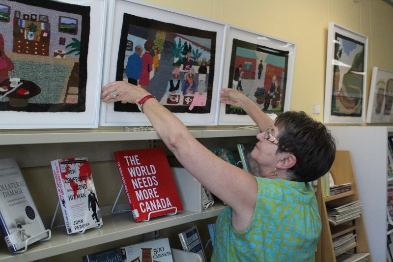 Didsbury library clerk Helen Johnson helps put up and straighten one of the woven tapestries created by Liv Pederson. The tapestries are part of the loom art exhibit on now