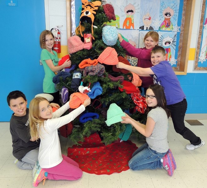 Kids smile beside the mitten tree.