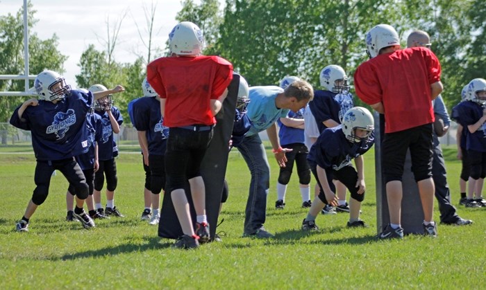 Coach Rob Walker, head coach of the Cyclones peewee team, works with Dylan Teskey-Smith on a three-point stance.