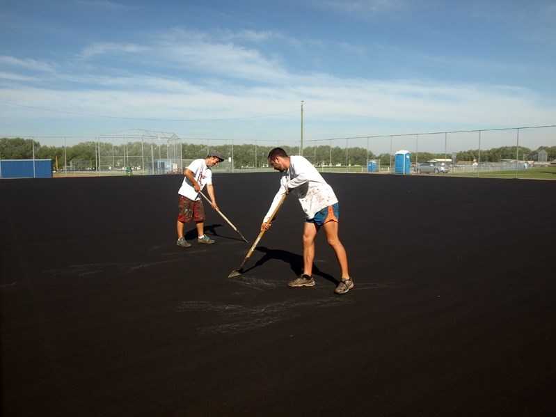 Piotr Burek (right) and Greg Kozlowski, employees of Calgary&#8217;s Tomko Sports Systems, work on the new surface of the Innisfail Tennis Courts on Aug. 14. It is the first