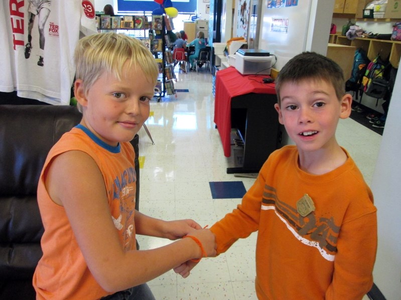 Seth (left), a Grade 4 student at Chinook Center School, ties a piece of orange yarn around the wrist of Grade 2 student Alex.
