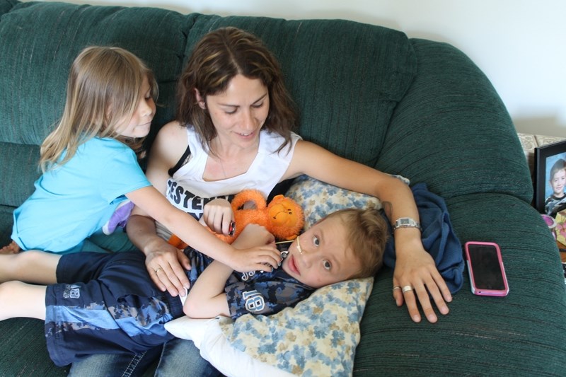 Five year-old Kylie watches as Kim Tucker cuddles seven yearold Gage Daoust in their Red Deer home. Gage returned hom from hospital last week.