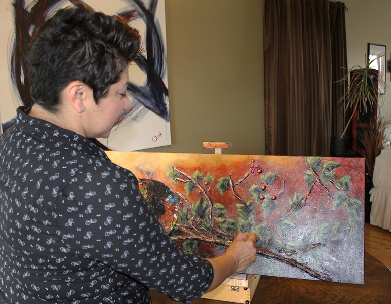 Mexican-born Innisfail artist Osi Cruz-Lahtinen puts on finishing touches to a recent painting-sculpture in her home studio.