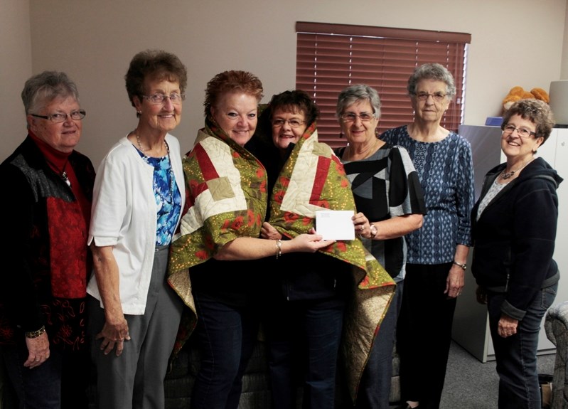 Linda Gurndersen (left), Linda Morgan (second from left), Ina Kooy (third from right), Mary Dyck (second from right), and Karen Carr (right) present a quilt from the Sew And