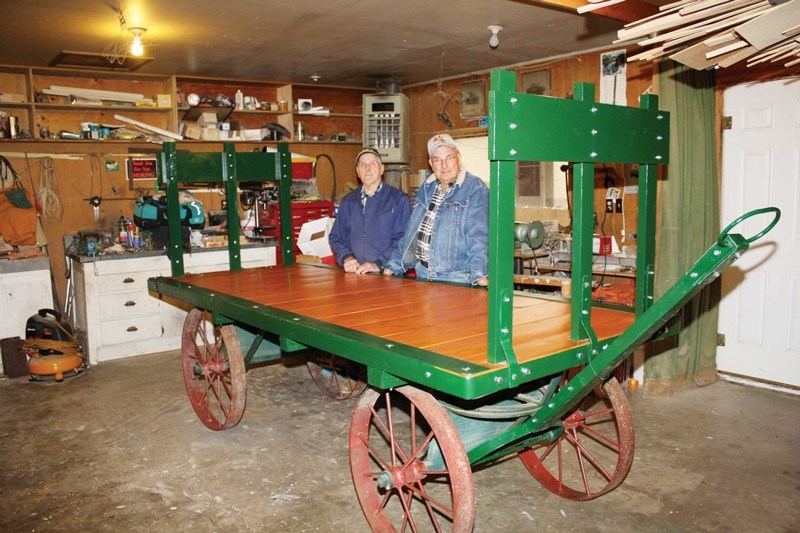 Merle Goddard (left) and Dale Saby stand beside the vintage luggage cart they recently restored.