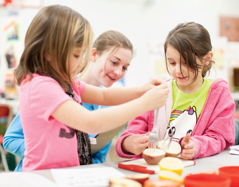 Ecole Olds Elementary School students Chloe Heppner, left, and Aaliyah Mossip, right, show their project to Olds High School student Jayna Wright during a science fair at the 