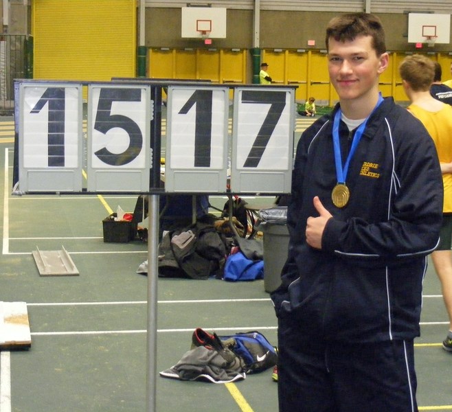 Andreas Troschke, a Grade 9 student at Olds High School, stands beside a sign indicating the record-breaking distance he threw in the 16-pound weight throw event at the