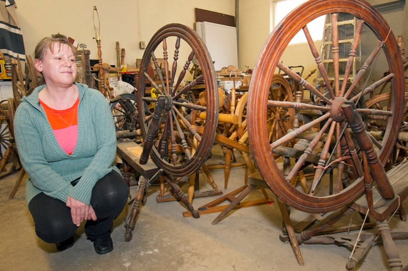 Chantal Marchildon, program coordinator for the Mountain View Museum and Archives in Olds crouches among some of the spinning wheels recently donated to the museum in a