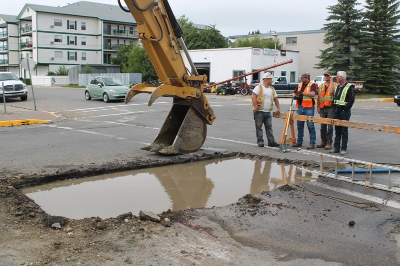 Workers stand beside an excavation hole filled with water at the intersection of 51 Avenue and 51 Street. A water line at the intersection was ruptured on the morning of July 