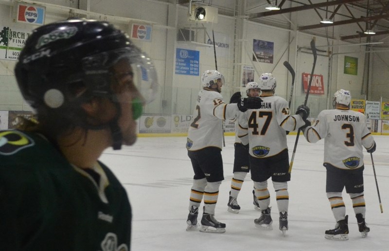 An Okotoks Oiler skates by as Grizzlys teammates gather to celebrate a goal Nov. 22.