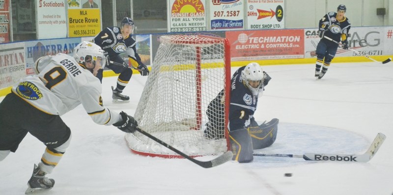 Grizzlys forward Chris Gerrie tries to flip the puck into the slot from behind the net while Calgary Mustangs goaltender Ravi Dattani tries to block it and guard the net