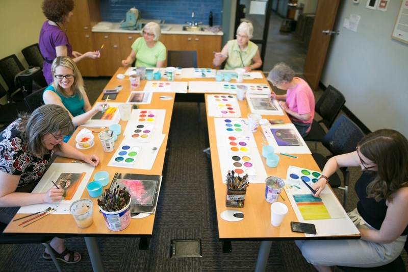 Participants in a monoprint workshop at the Olds Municipal Library paint on acrylic glass, using images underneath as guides.