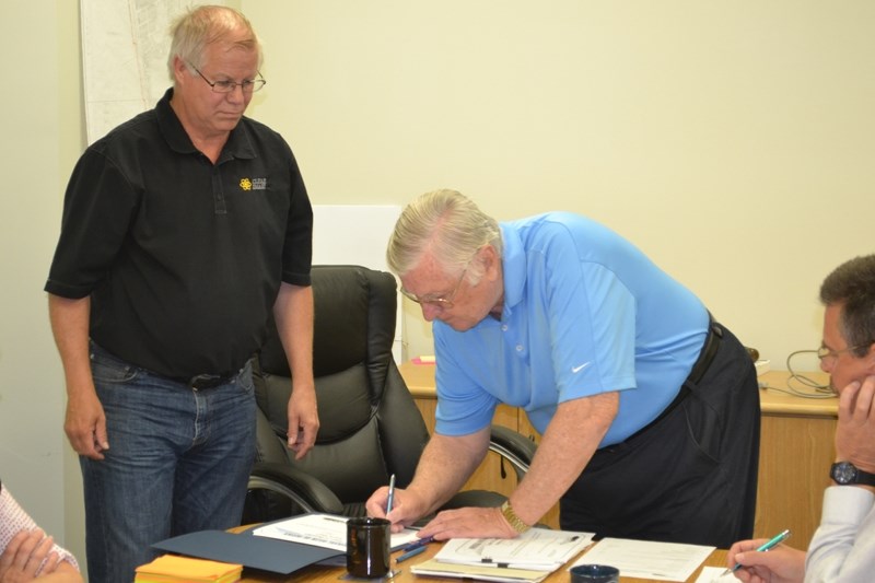 Bowden mayor Robb Stuart, left, looks on as Coun. Earl Wilson signs documents proclaiming him the town&#8217;s deputy mayor.
