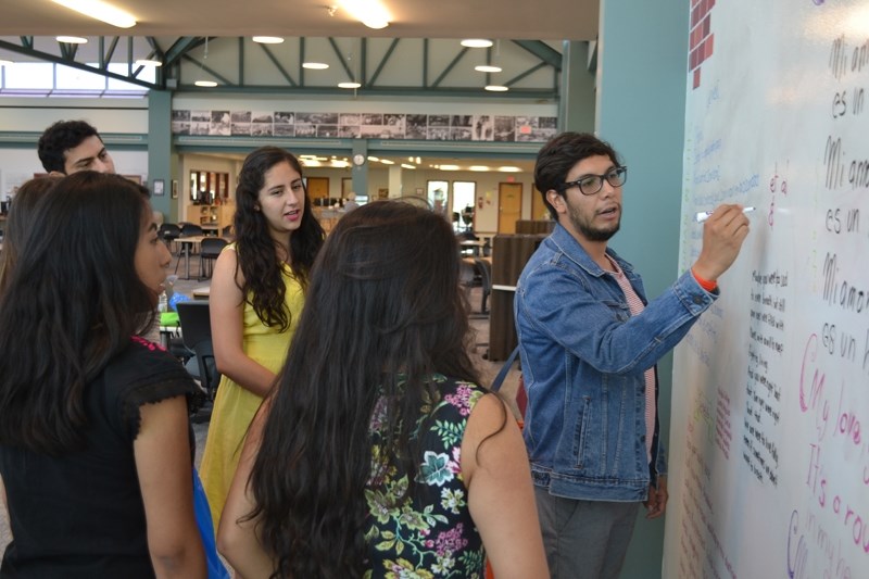 Mexican students and instructor-translators take turns writing and clarifying poems they wrote on a wall of the Olds College Learning Resources Commons during their