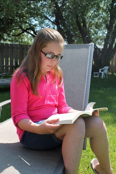 Nine-year-old Gemma Smyth, who received special lenses in February to help her read after being diagnosed with Irlen syndrome, enjoys a book in her backyard on Aug. 11.