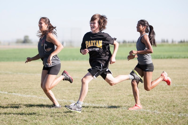 From left: Olds High School students Janelle Graham, Leif Aitken and Anushree Patel sprint across the Normie Kwong football field during a cross country practice on Sept. 12.
