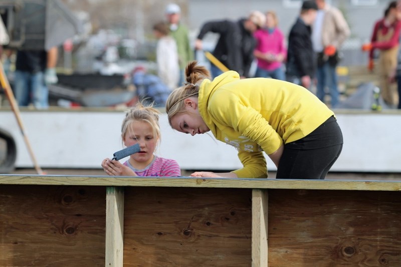 Callie (left) and Cheyenne Cocke paint the boards lining the new outdoor ice rink during the Community Action Park build day in Bowden on Oct. 26.