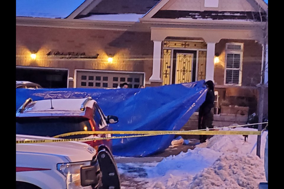 Police officers and forensic investigators screen use a tarp as a screen to obscure a dead body in front of the house in Mount Albert on Feb. 6.