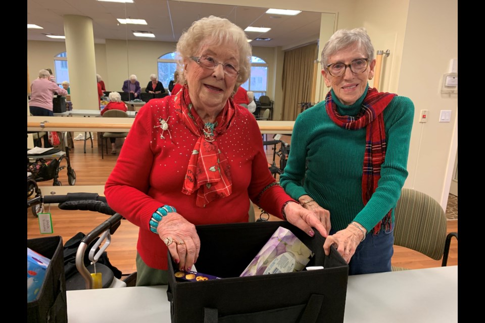 Amica residents Dolly Borthwick and Grace Campbell don Christmas colours to pack  goodwill baskets on Dec. 4. Debora Kelly/NewmarketToday