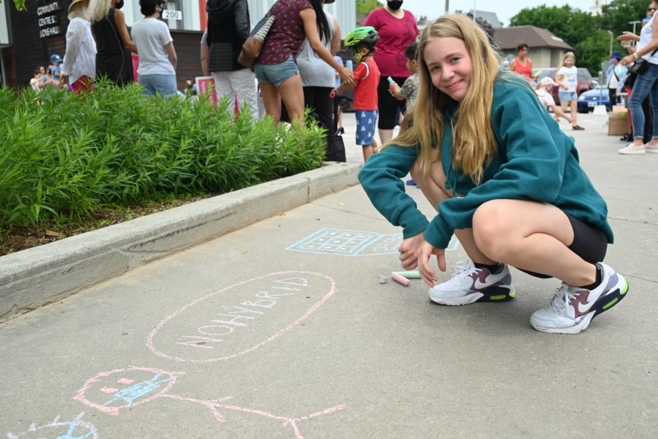 Grade 8 student Grace Lodoen  makes a chalk drawing opposing hybrid learning, at the Riverwalk Commons July 24. 