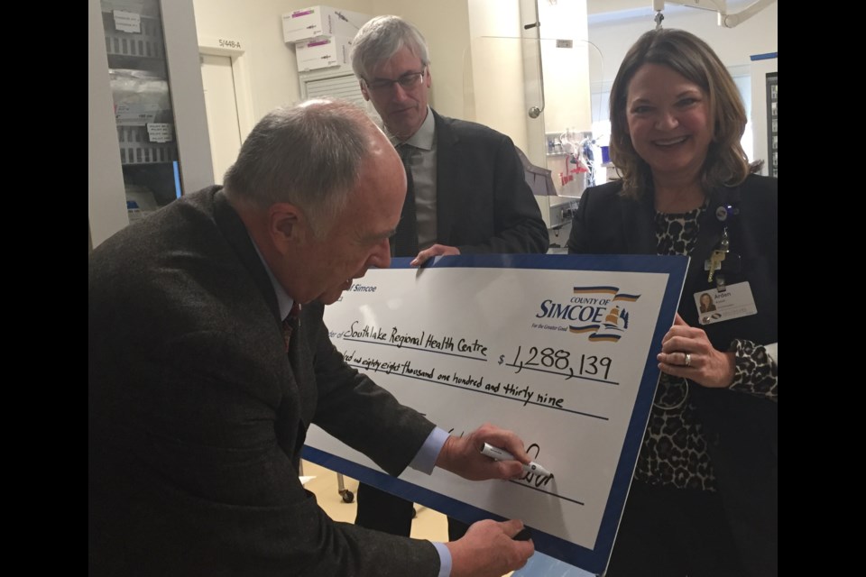 County of Simcoe Warden George Cornell "signs" the $1.288-million cheque for Southlake Regional Health Centre today, while Bradford Mayor Rob Keffer and Southlake President and CEO Arden Krystal look on. Debora Kelly/NewmarketToday