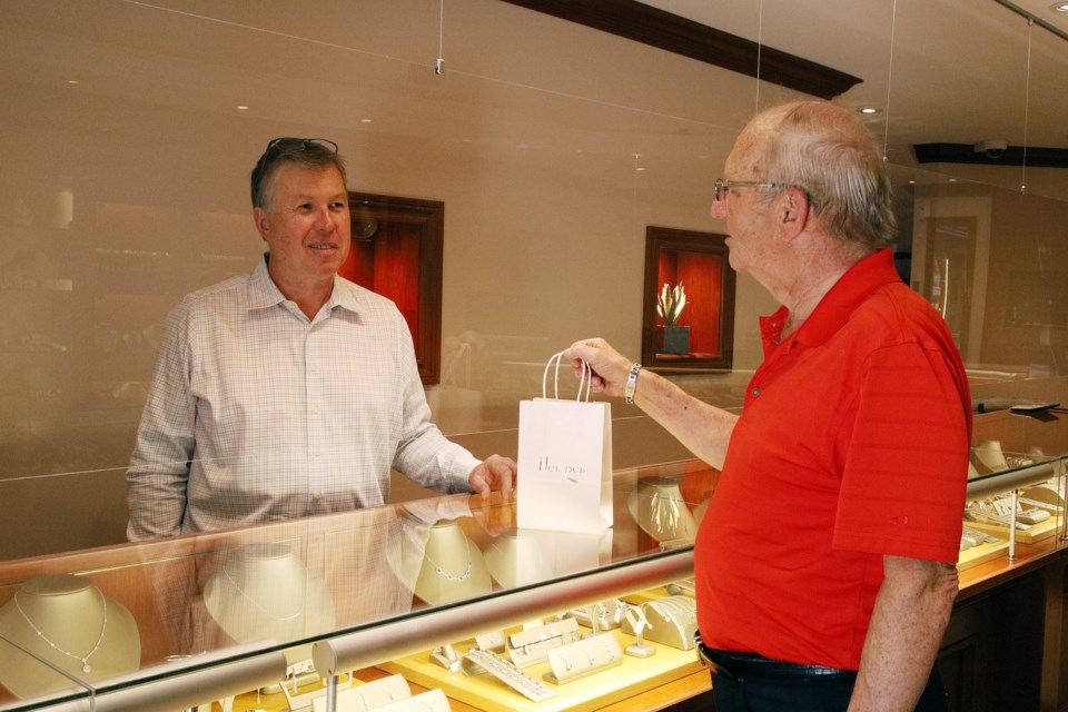 Tom Hempen of Hempen Jewellers on Main Street talks to customer Rick Metcalfe on the other side of plexiglass shields installed over all the counters.  Greg King for NewmarketToday