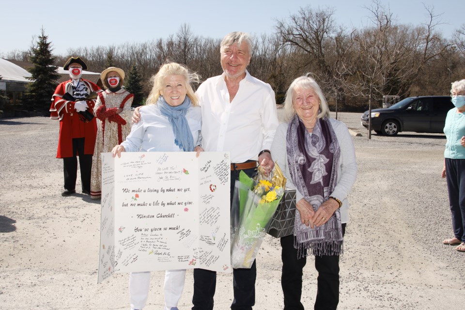 Lois Brown presents a giant farewell card to Ole and Lisbeth Madsen, as friends gathered outside Madsen's Greenhouse for a drive-by parade Sunday afternoon.  Greg King for NewmarketToday