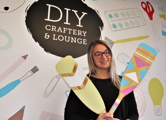 Kelsey Cutinello, owner of DIY Craftery and Lounge in Sudbury, poses with a pair of painted canoe paddles made at the craftery. Those are among many craft projects corporate groups can book to host a teambuilding event. (Karen McKinley photo)