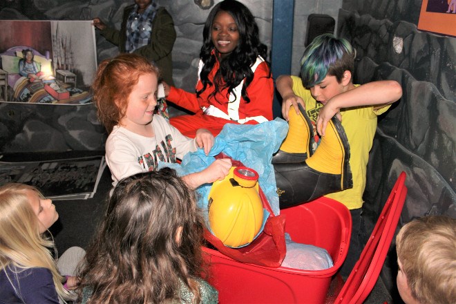 During the book launch of Underground! My Mining Adventure, author Theresa Nyabeze invited some of the Grade 2 and 3 students attending the event to volunteer for activities as she read the book, such as holding up large illustrations, which were illuminated by a miner's helmet lamp, and help unwrap a giant red box, just like in the book, where they found child-sized mining clothes and an old-fashioned miner's lunchbox.
Karen McKinley photo
