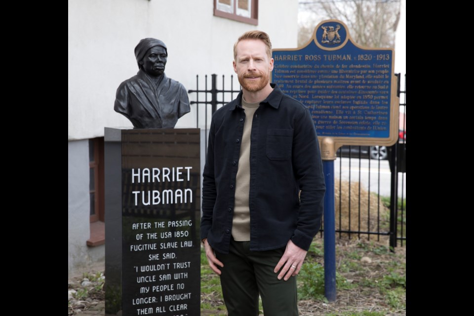 Amazing Race Canada host Jon Montgomery stands next to a bust of Harriet Tubman in St. Catharines
