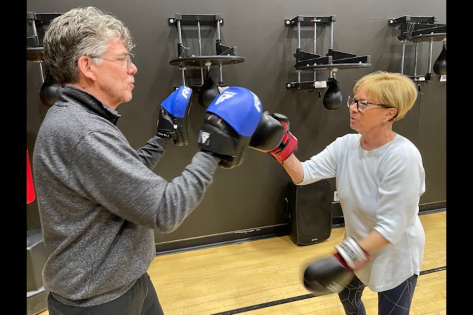 Volunteer Rick Mills lends a helping hand to Peggy Thorne as she boxes during a Rock Steady Boxing session..