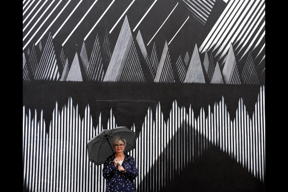 Highland Optical owner Sharyn Webber takes in a striking black and white mural by artist Kari Kristensen in North Vancouver's Edgemont Village, part of the Vancouver Mural Festival running until Aug. 22, 2021.