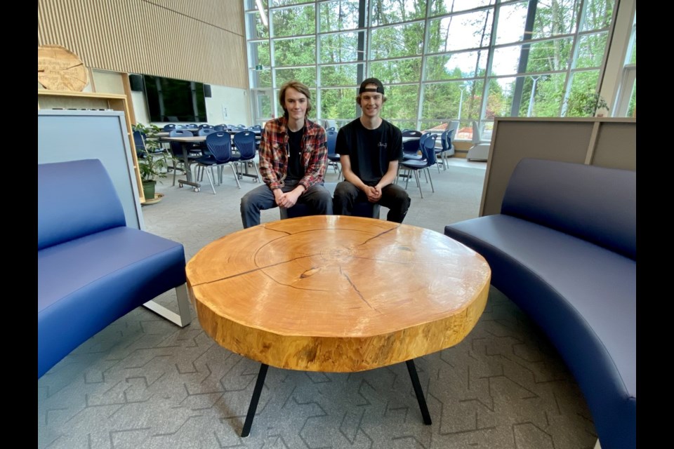 École Argyle Secondary graduates Oscar and Theo Derban sit at the coffee table Oscar crafted from a  fallen 280-year-old fir tree. They hope the table will spark discussions about British Columbia’s old-growth forests for years to come in the school's library.