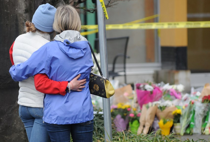 Two women pause at a growing memorial at the Lynn Valley library Sunday, March 28, one day after a man killed one person and injured six others in a stabbing attack. 