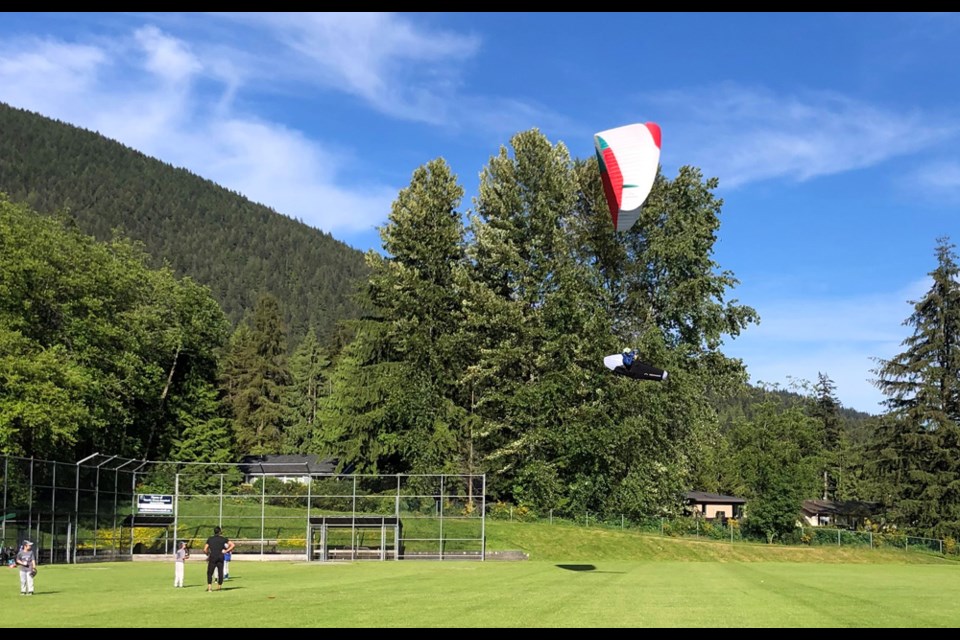A paraglider comes in for a landing on the upper field of North Vancouver's Cleveland Park as youth baseball players practise nearby, on June 8, 2022. 