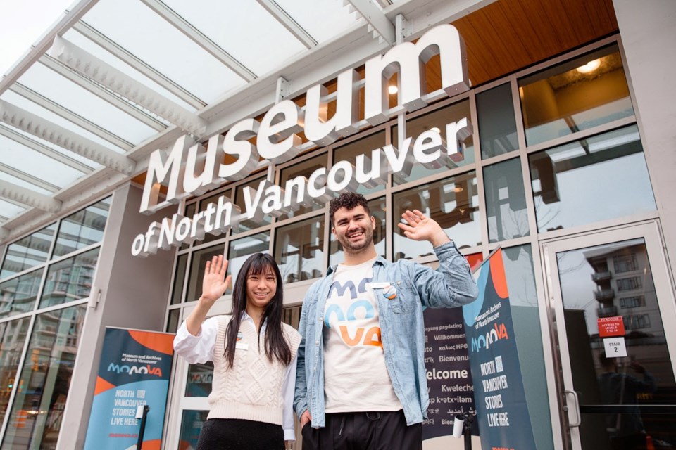 Two guest services representatives, one female and one male, offering a friendly wave at the front entrance of MONOVA: Museum of North Vancouver with signage overhead.