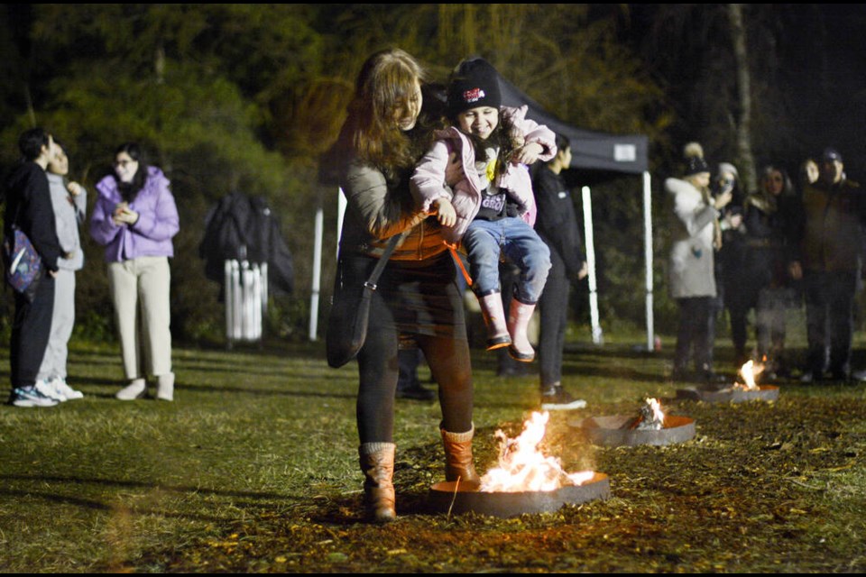 A woman lifts a smiling young girl with pink rain boots over a fire pit. | Nick Laba / North Shore News 