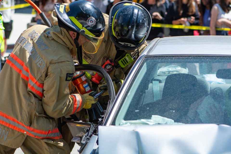 Two firefighters use the Jaws of Life to rend the passenger door off one of the cars during a mock crash demonstration at Ecole Handsworth Secondary Friday. | Nick Laba / North Shore News 