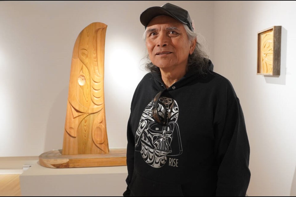 Squamish artist Xwalacktun, flanked by two of his pieces being shown at West Vancouver’s Ferry Building Gallery, has a message he wants people to take from the Reflecting on Home show, which runs until Oct. 15. | Brent Richter / North Shore News 