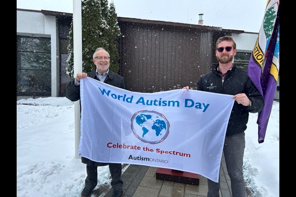 Fort Frances Mayor Andrew Hallikas, left, and municipal planner John Burrows pose with a World Autism Day flag in fort Frances on April 2, 2025.