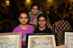 two girls and one boy holding plaques | Nowruz Bazaar for Iranian New Year; Rojean. Layla & Romina, Photo Credit: Janet Bedford | Janet Bedford