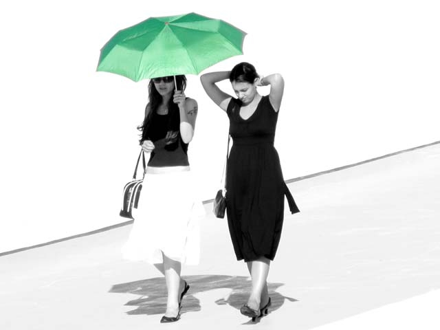 two women walking under a green umbrella | Photo credit: betim