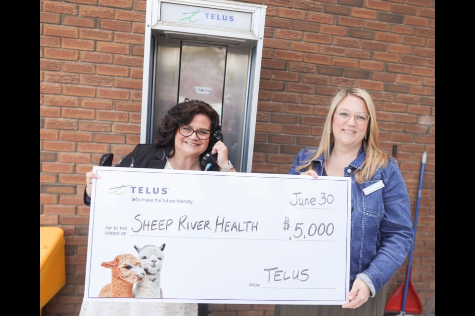Telus representative Theresa Lynn (left) presents Sheep River Health Trust executive director Andrea Mitchell with a cheque for $5,000 at a ceremony to mark the decommissioning of Okotoks' last payphone on June 30.
